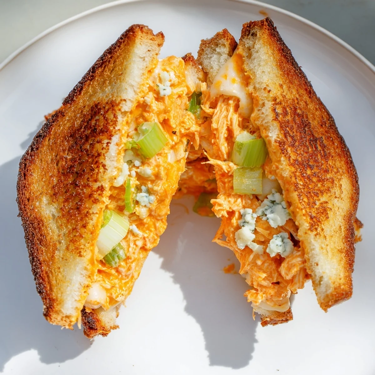 Melted mozzarella oozing from a gooey Buffalo Chicken Grilled Cheese sandwich, a delicious lunch.