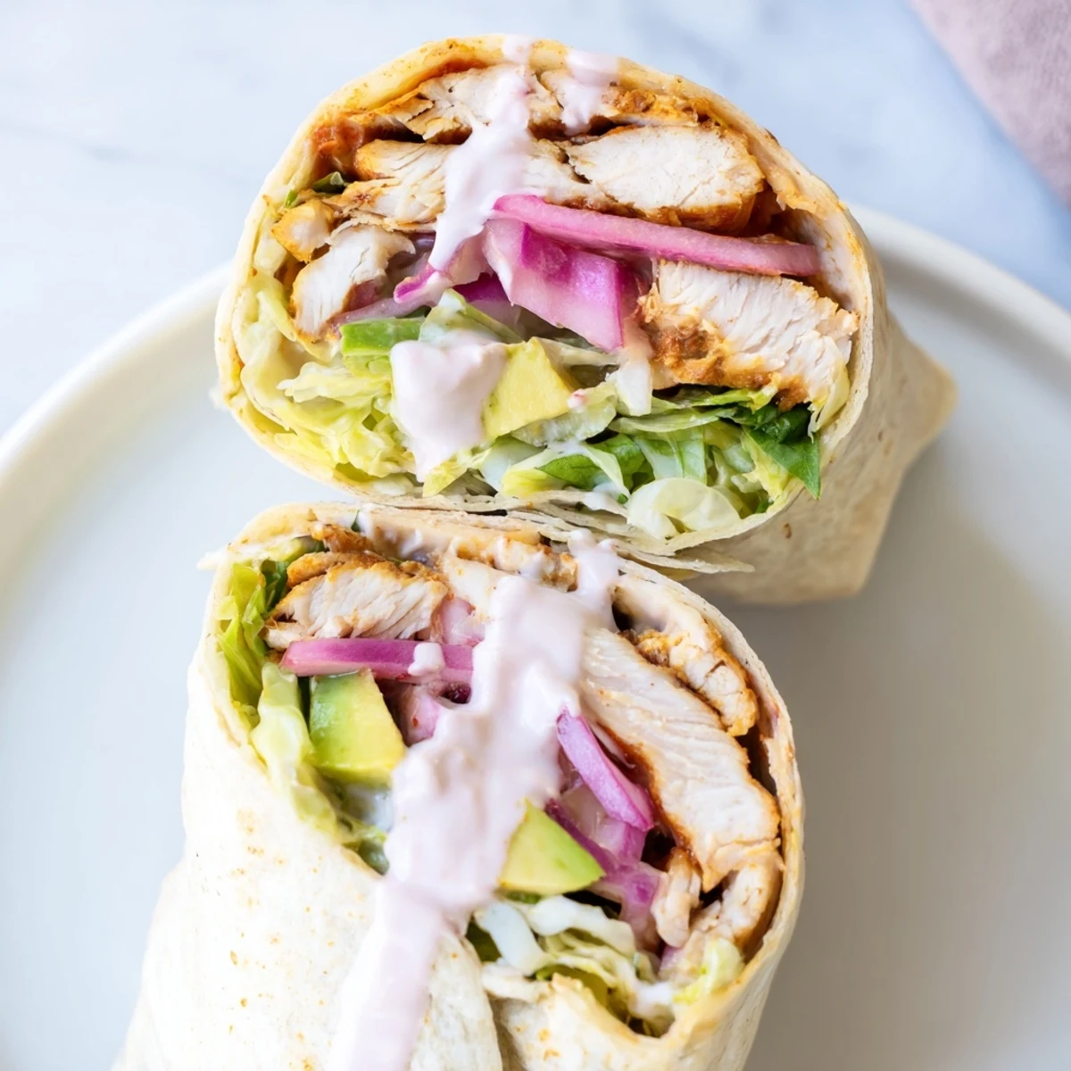 Golden-brown chipotle chicken strips, creamy avocado slices, and crisp lettuce fill a soft flour tortilla, drizzled with tangy Greek yogurt sauce.