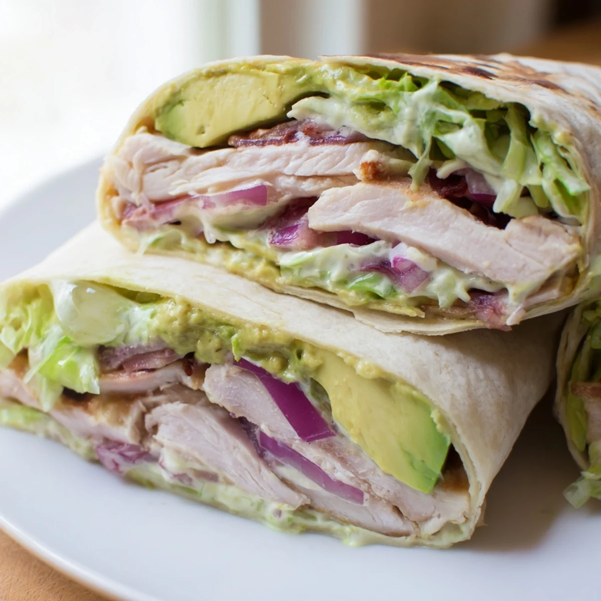 Close-up of a sliced Smoky Chipotle Chicken Wrap revealing layers of smoky chicken, creamy avocado, and shredded lettuce with a dollop of yogurt sauce.