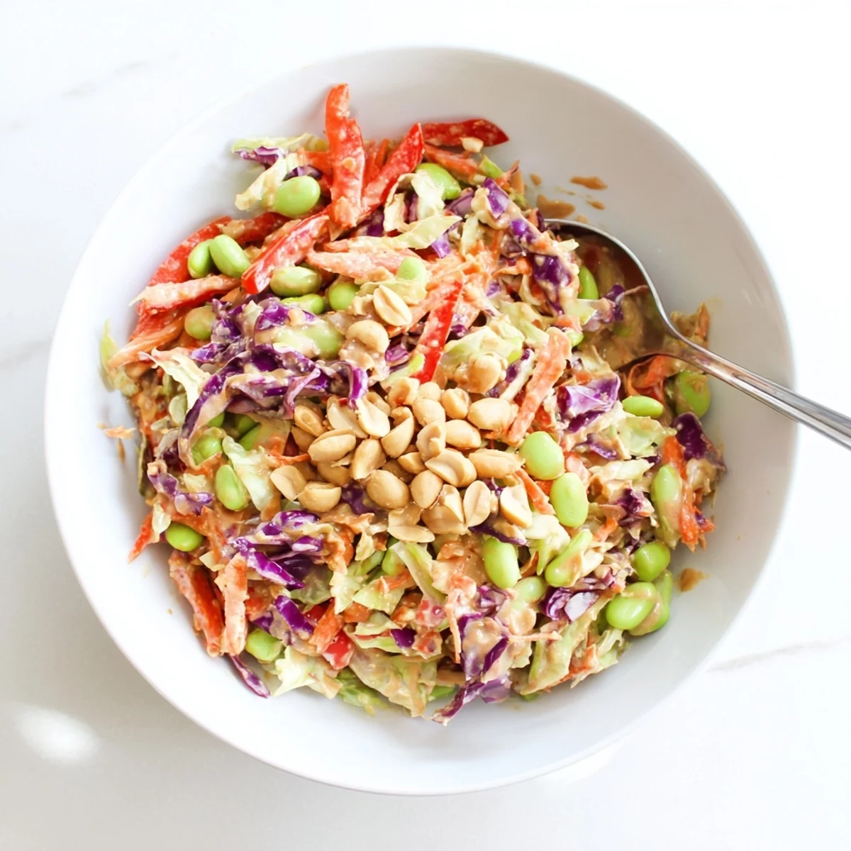 A vibrant Crunchy Thai Peanut Salad with shredded purple cabbage, carrots, and edamame in a creamy peanut dressing, topped with chopped peanuts.