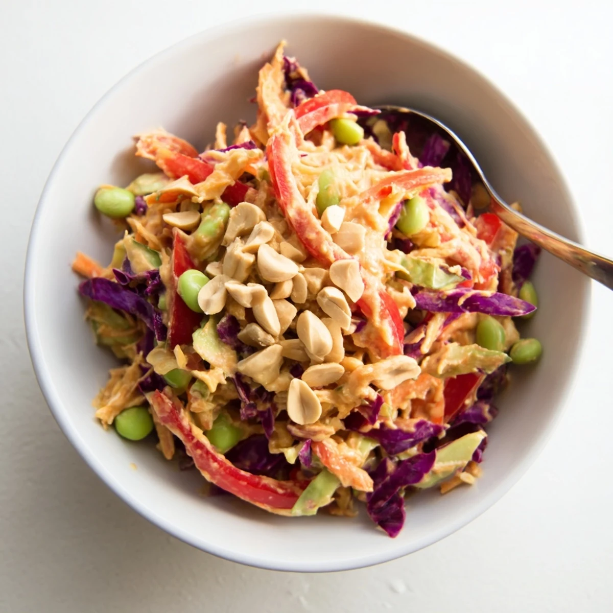 Colorful Crunchy Thai Peanut Salad served in a white bowl with lime wedges, ready for a refreshing vegetarian meal or side dish.