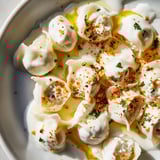 These golden-brown Turkish cheesy manti appear nestled in creamy yogurt, ready to be enjoyed.
