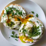 Turkish-American Çılbır Eggs Benedict: Vibrant fresh herbs garnish the decadent, flavorful breakfast dish.