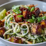 A close-up of creamy chili crisp dressing coating spiralized cucumbers and wheat noodles in a vibrant bowl.