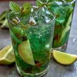 A vibrant virgin green mojito with fresh lime, mint, and cucumber slices, served over ice with sparkling water for a refreshing summer drink.