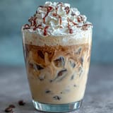 Creamy vanilla frappuccino with cold brew ice cubes, topped with whipped cream and vanilla bean drizzle in a tall glass.