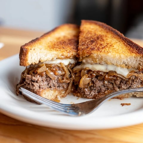 Cast-Iron Patty Melts sizzling in a cast-iron skillet, showcasing a perfect golden-brown crust.