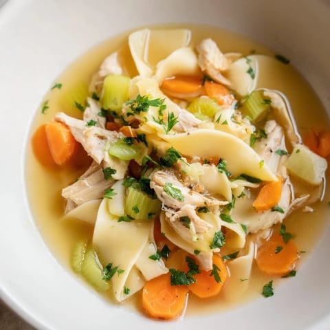 Steaming bowl of Classic Chicken Noodle Soup with tender chicken and fluffy egg noodles.