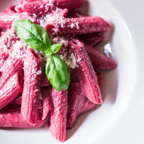 Vibrant Pink Pasta with Beet Cream swirls in a bowl, garnished with fresh basil and Parmesan, ready to serve.