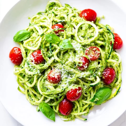 Freshly spiralized zucchini noodles coated in creamy avocado pesto, topped with juicy halved cherry tomatoes.