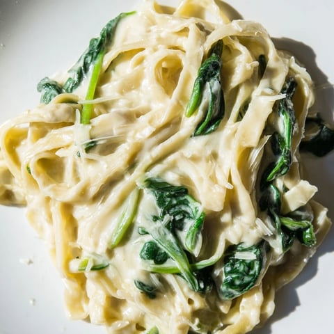 Steaming bowls of creamy garlic spinach pasta topped with extra Parmesan and fresh parsley garnish.
