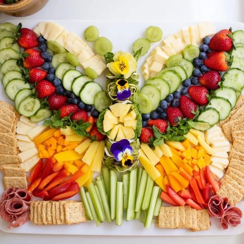 A stunning Butterfly Summer Board, overflowing with summer flavors, includes vibrant fruit and artisan cheeses.