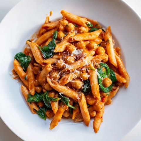 A close-up of Creamy Tuscan Chickpea Pasta, showcasing vibrant spinach and juicy tomatoes in a velvety garlic parmesan sauce.