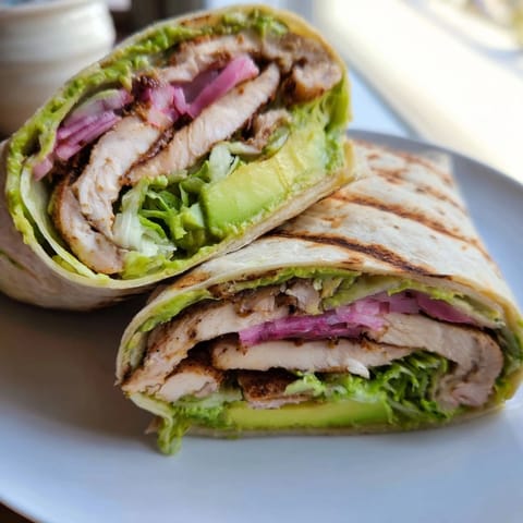 Freshly assembled Smoky Chipotle Chicken Wrap halves show juicy chicken, diced red onion, and vibrant tomato nestled in a warm, pliable tortilla.