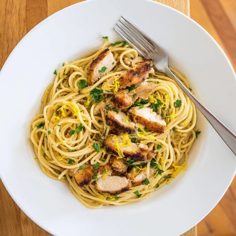 Spaghetti twirls in a glossy lemon butter sauce with seared chicken, bright zest, and fresh parsley.  