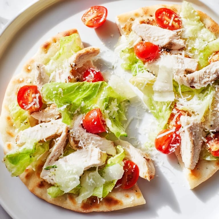 Sliced Chicken Caesar Flatbread served with cherry tomatoes, extra dressing, and fresh pepper.