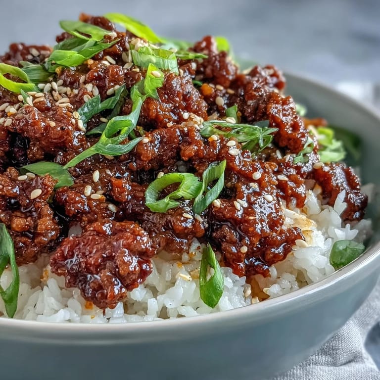 A close-up of a delicious Easy Korean Beef Bowl with vibrant carrots and cucumber, drizzled with spicy sauce and ready to enjoy.