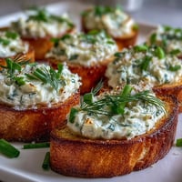 Elegant cream cheese and herb crostini board with golden toasted baguette slices topped with herbed spread and fresh herbs.  