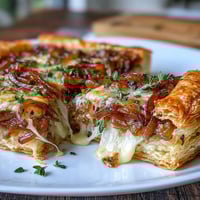 Golden caramelized onions and melted Gruyère cheese on flaky puff pastry, garnished with fresh thyme for a savory French onion tart.